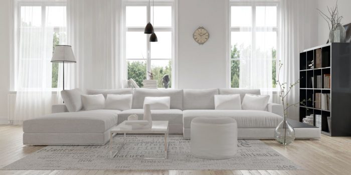 Modern spacious lounge or living room interior with monochromatic white furniture and decor below three tall bright windows with a dark bookcase accent in the corner