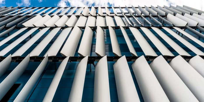 The facade of a modern building with an innovative facade made of automatic, movable blinds against the background of blue sky with clouds.